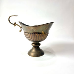 May include: A vintage brass bowl with a decorative handle and a fluted base. The bowl has a worn, antique finish.