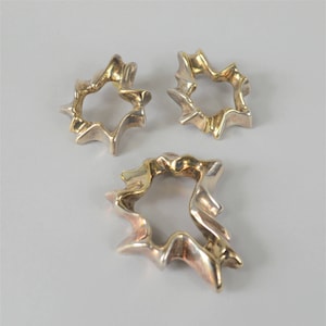 May include: Three gold-toned metal rings with an irregular, organic shape. The rings are all different sizes and have a slightly textured surface.
