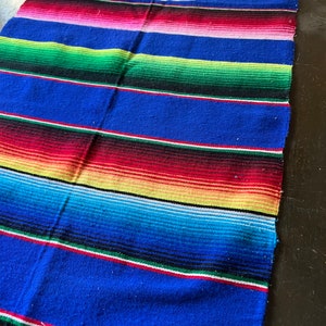 May include: A colourful Mexican blanket with stripes of red, pink, blue, green, yellow and white.