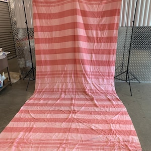 May include: A large pink and white striped fabric backdrop. The fabric is hanging from a wooden dowel rod.