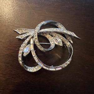 May include: A silver brooch with a swirling design set with clear rhinestones.