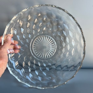 May include: A large, clear glass serving bowl with a diamond pattern and a smaller, circular, patterned center. The bowl is made of thick glass and has a slightly wavy edge.