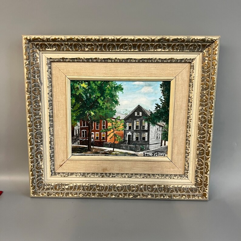 May include: Framed painting of a street scene with three houses, two trees, and a blue sky. The houses are painted in shades of red, gray, and white. The trees are green and the sky is blue with white clouds. The painting is signed "Ian Selmas" in the lower right corner.