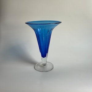May include: A blue glass vase with a flared opening and a clear glass base. The vase has a ribbed design.