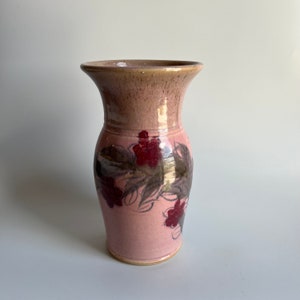 Könnte beinhalten: Eine rosa Keramikvase mit einem Blumendesign. Die Vase hat eine breite Öffnung und einen schmalen Boden. Die Blumen sind in Rot- und Brauntönen bemalt.