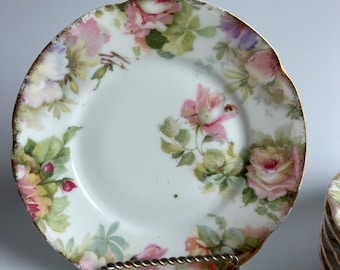 May include: A white porcelain plate with a gold rim and a floral design featuring pink roses and green leaves.