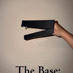 Puede incluir: Objeto negro y angular sostenido contra una pared texturizada. El objeto parece estar hecho de un material rígido, con un borde dentado en un lado. El texto en la parte inferior dice "The Base:"