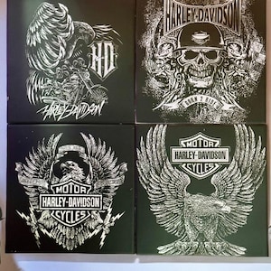 May include: Four black square wall art pieces with white Harley-Davidson graphics. Designs include an eagle, skull, motorcycle, and the Harley-Davidson logo. The text "Born 2 Ride" is also visible.