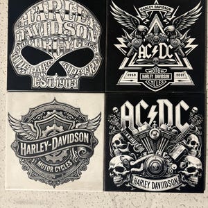 May include: Four square ceramic coasters with Harley-Davidson and AC/DC designs. The coasters feature black and white graphics, including skulls, wings, and motorcycle engine illustrations. The Harley-Davidson coasters have the text "EST 1903".
