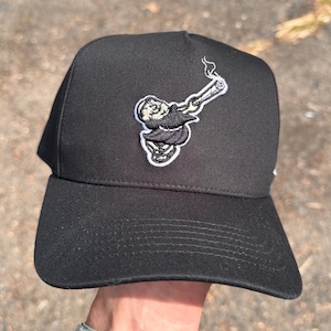 Pode incluir: Bon&eacute; de beisebol preto com aba reta. O bon&eacute; apresenta um patch bordado de um personagem de desenho animado fumando um cigarro enrolado. A figura est&aacute; vestindo uma t&uacute;nica. O bon&eacute; &eacute; feito de tecido dur&aacute;vel.