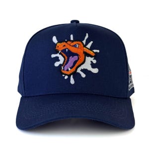 Pode incluir: Boné de beisebol azul marinho com um design bordado de dragão laranja e roxo e um efeito de respingo branco. O boné tem uma aba curva e um botão na parte superior. O design está na frente.