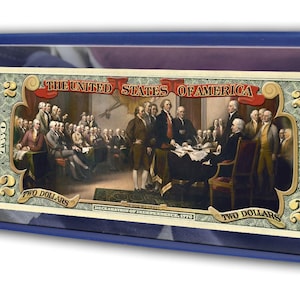 May include: A framed two-dollar bill featuring a historical painting of the signing of the Declaration of Independence. The frame is blue, and the bill is displayed alongside text detailing the event.