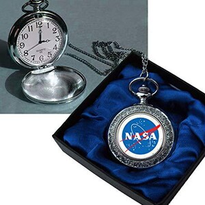 May include: A silver-toned pocket watch with a white face and black numerals, open to reveal the time. A second pocket watch with the NASA logo is displayed in a black box with blue satin lining. The watch has a chain.
