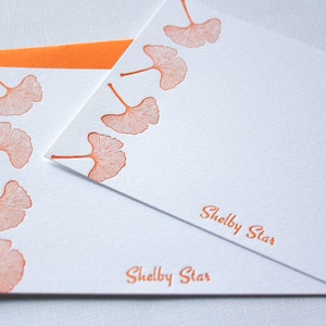 May include: Two white stationery cards with orange ginkgo leaf designs and the text "Shelby Star" printed on each card.