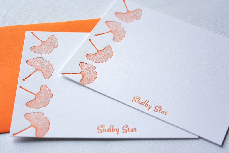 May include: Two white stationery cards with orange ginkgo leaf designs and the text "Shelby Star" printed on each card.