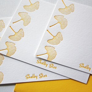 May include: Three white note cards with a gold ginkgo leaf border and the text "Shelby Star" printed on each card.