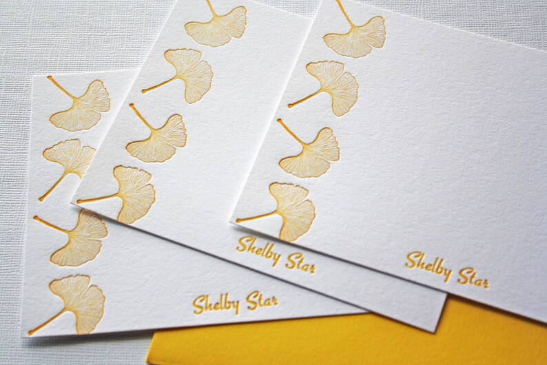 May include: Three white note cards with a gold ginkgo leaf border and the text "Shelby Star" printed on each card.