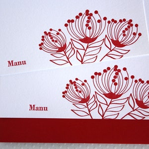May include: Two white cards with red ink. The top card has a red floral design with the word "Manu" printed on the bottom. The bottom card has a red floral design with the word "Manu" printed on the bottom and a red border.