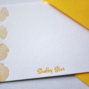 May include: White stationery card with a yellow envelope. The card has a border of five gold ginkgo leaves and the text "Shelby Star" in gold lettering.