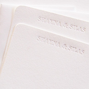 May include: Two white cards with the text "Shayna & Silas" embossed on them.