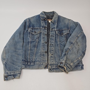 Könnte beinhalten: Eine blaue Jeansjacke mit klassischem Kragen, langen Ärmeln mit geknöpften Manschetten und einer Knopfleiste vorne. Das Kleidungsstück verfügt über zwei Brusttaschen mit geknöpften Klappen, sichtbare Verwaschungen und abgenutzte Kanten.