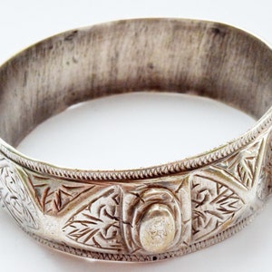Peut inclure: Un bracelet jonc argenté orné de motifs gravés complexes. Le bracelet présente une large bande avec une surface texturée et des éléments décoratifs. Le design comprend des motifs de feuilles et une forme ovale centrale. Largeur d'environ 6 cm.