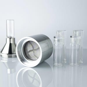 May include: A selection of scientific equipment in silver and glass. The image shows a cylindrical metal component with a mesh filter, small glass vials, and a conical glass and metal device. The items are arranged on a reflective surface.