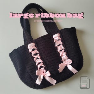 Może przedstawiać: Czarna torba typu tote wykonana na szydełku z różowymi wstążkami. Torba ma duży, otwarty design z różowymi akcentami wstążkowymi z przodu. Tekst "large ribbon bag" jest wyświetlany na różowo nad torbą.