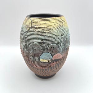 May include: A handcrafted ceramic vase with a textured surface and a unique design. The vase features a black rim, with a gradient of colors from yellow to blue. The lower portion has a brown, wood-like texture, and the middle section has a landscape design.