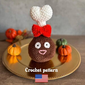 May include: A brown crochet turkey leg with a white bone, red bow, and smiling face. The turkey sits on a gold plate with miniature pumpkins. The text "Crochet pattern" is displayed below the turkey.