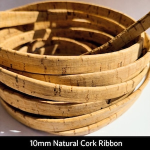 Puede incluir: Rollo de cinta de corcho natural de 10 mm. La cinta marrón claro tiene una superficie texturizada y veta visible. La cinta enrollada muestra varias capas. El texto "10mm Natural Cork Ribbon" está en la parte inferior de la imagen.