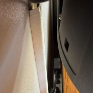 May include: A close-up view of a white cable management system installed on a wall. A black cable is routed through the system, alongside a black TV. The wall has a textured surface.