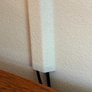 May include: A white, textured, rectangular object is mounted on a textured wall. Two black, parallel lines extend from the bottom of the white object. A wooden surface is visible at the bottom of the image.
