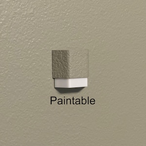 May include: A paintable, two-tone object with a textured, grey top and a white base. The word "Paintable" is printed in black below the object. The object is mounted on a light beige wall.
