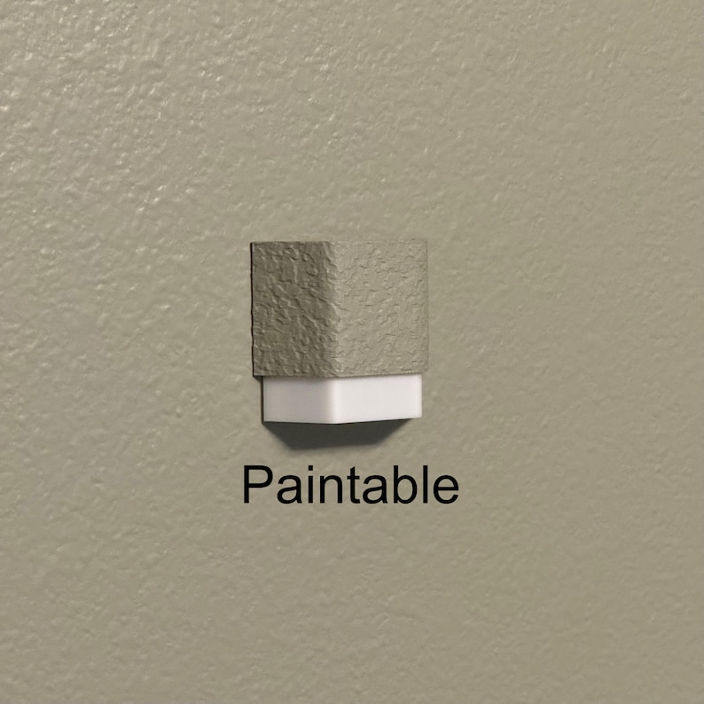 May include: A paintable, two-tone object with a textured, grey top and a white base. The word "Paintable" is printed in black below the object. The object is mounted on a light beige wall.