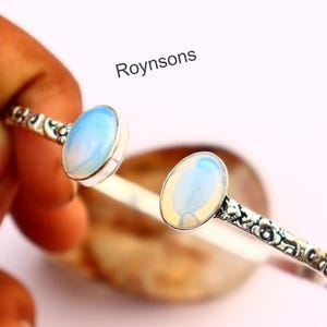 May include: Silver bracelet featuring two oval opalescent stones. The band has a decorative floral pattern. The text "Roynsons" is visible in the image.