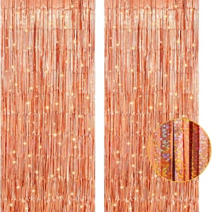 May include: Two rose gold metallic fringe curtains. The curtains are made of long, thin strips of shiny material, creating a shimmering effect. The close-up shows the texture and the light reflecting off the surface. Ideal for party decorations.
