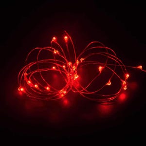 May include: A string of thin, flexible wire lights featuring small, glowing red LED bulbs. The wire is coiled into two circular loops, creating a continuous, illuminated display of bright red light points against a dark, black background.