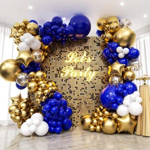 May include: A party backdrop featuring a gold sequin wall with the words "Let's Party" in neon. The backdrop is decorated with gold, blue, white, and clear balloons, including star-shaped balloons. The balloons are arranged in an arch shape.