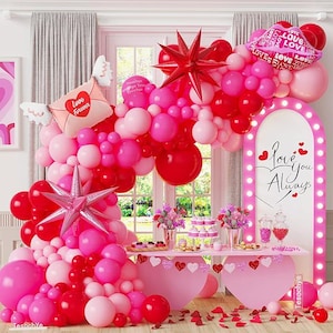 May include: A festive Valentine's Day party scene with a pink and red balloon arch, a table with desserts, and a sign that says "Love You Always." The balloons include star and heart shapes.