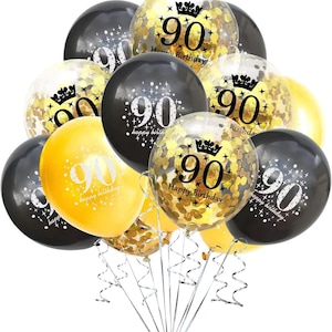 May include: A cluster of black, gold, and clear balloons, celebrating a 90th birthday. Some balloons are filled with gold confetti. The balloons have the number 90 printed on them, along with the words "Happy Birthday". Silver ribbons are attached.