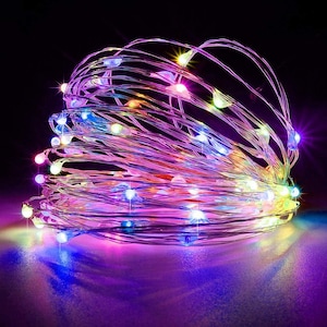 May include: A coiled strand of thin, flexible silver wire featuring numerous small, multi-colored LED lights. The lights emit a vibrant glow in shades of blue, purple, pink, yellow, and green, creating a dense, luminous cluster against a dark background.