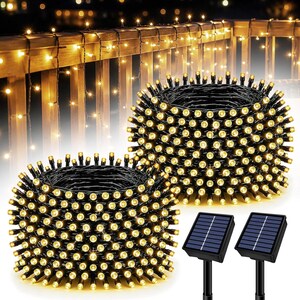 May include: Two coils of black wire string lights featuring warm white LED bulbs. Each coil is paired with a black solar panel mounted on a stake. The lights are shown illuminated in a circular pattern, with additional lights draped on a railing.