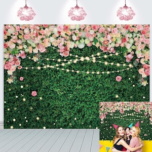 May include: A backdrop featuring a green hedge wall adorned with pink and white roses, fairy lights, and a smaller image of the same scene with three women. Overhead, three pink floral-shaped lights hang from the ceiling.