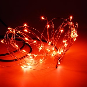 May include: A string of thin, flexible wire lights emitting a bright red glow. The lights are arranged in a tangled, circular cluster, with individual small LED bulbs spaced along the metallic wire, creating a vibrant and concentrated illumination.