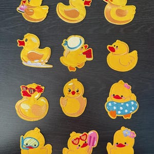 May include: A set of twelve yellow duck patches with embroidered details. Each duck has a unique design, including sunglasses, hats, and accessories. The patches are suitable for clothing or craft projects.