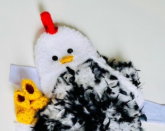 May include: A handmade chicken costume with a white plush head, black and white feather body, and yellow crochet booties. The chicken has a red comb and a yellow beak. The costume is designed for a baby or toddler.