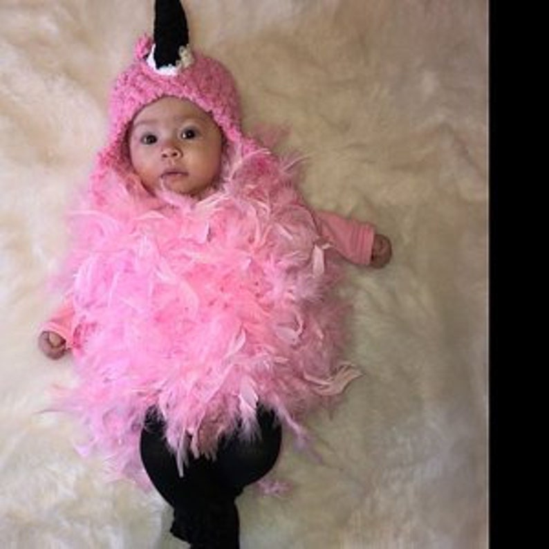 May include: A pink flamingo costume for a baby, featuring a crocheted hat with a black beak and pink feathers.