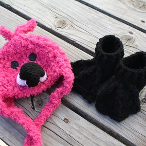 May include: A pink crocheted hat with a bear face and black crocheted booties.