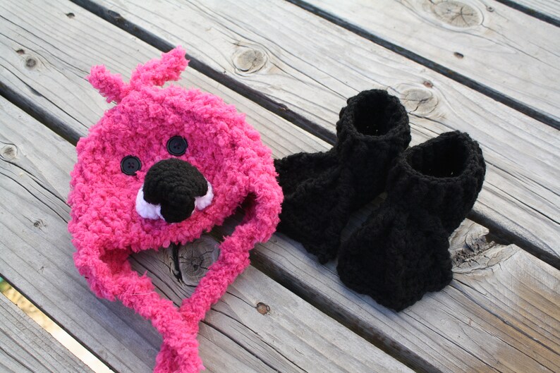 May include: A pink crocheted hat with a bear face and black crocheted booties.